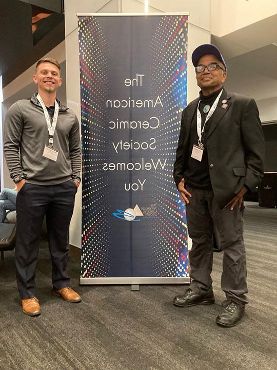 Two men standing in front of a sign