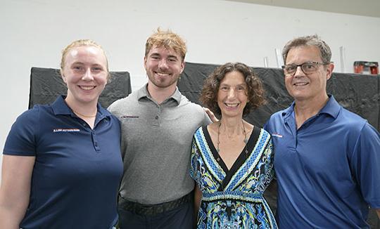 four people, two men and two women, standing side by side, smiling