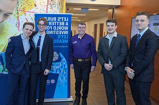 four young men in suits with professor in collared shirt, standing in a row smiling