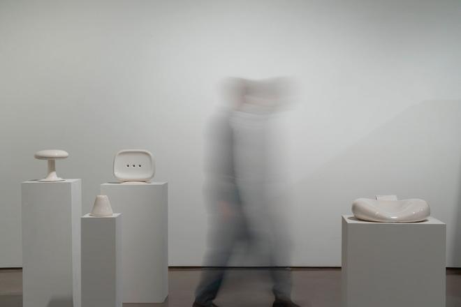 A person walking past a collection of white ceramic objects installed on white pedestals